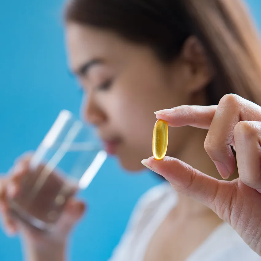 A woman prepares to take a golden supplement capsule with a glass of water